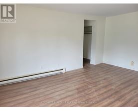 A room with wooden flooring and white walls, with a doorway leading to another room.