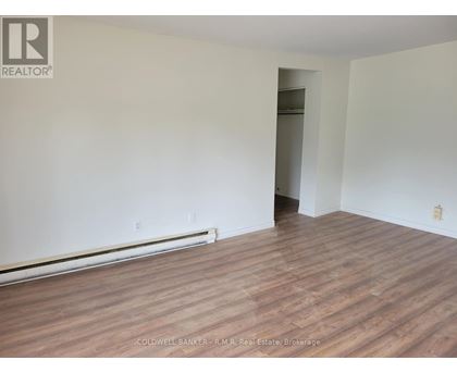 A room with wooden flooring and white walls, with a doorway leading to another room.
