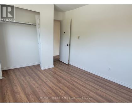 A room with wooden flooring and white walls, with a door and a closet.