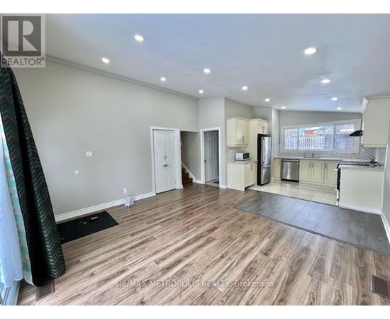 A spacious living room with hardwood flooring and a kitchen area in the background.