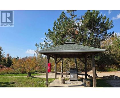 A gazebo with a picnic table and a grill is surrounded by trees.