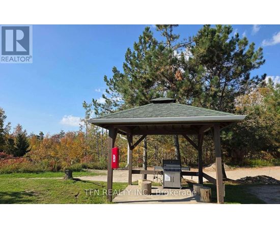 A gazebo with a picnic table and a grill is surrounded by trees.