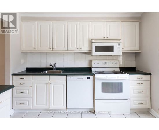 A white kitchen with a black counter top and white appliances.