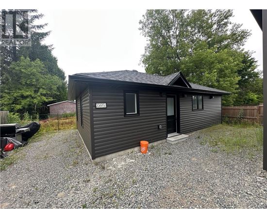 A small house with a black door and windows is surrounded by a gravel driveway.