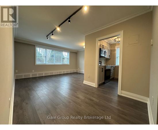 A spacious room with wood flooring and a kitchen area in the background.