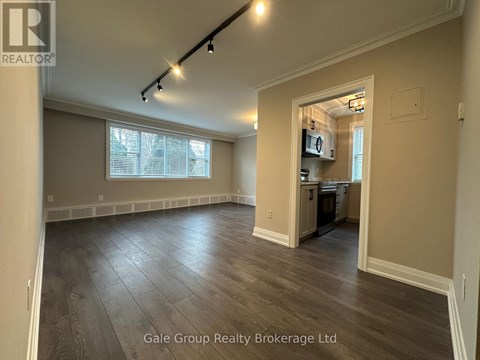A spacious room with wood flooring and a kitchen area in the background.