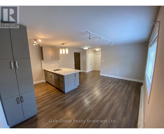 A spacious room with wooden flooring and a kitchenette area.