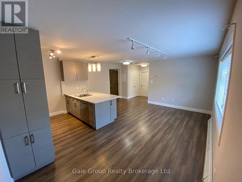 A spacious room with wooden flooring and a kitchenette area.