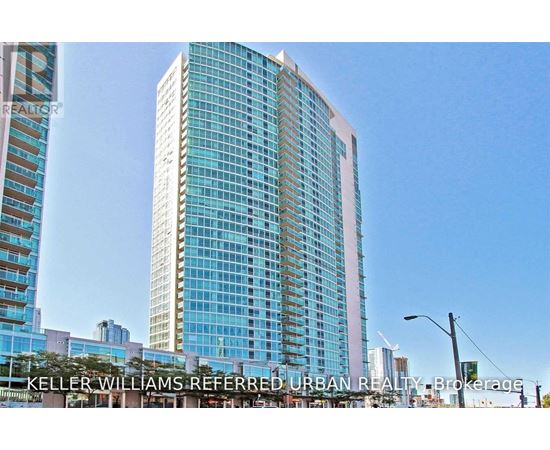 A tall building with a glass facade stands in front of other buildings.