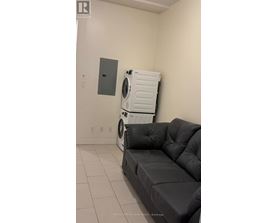 A black sofa in a room with a washing machine behind it.