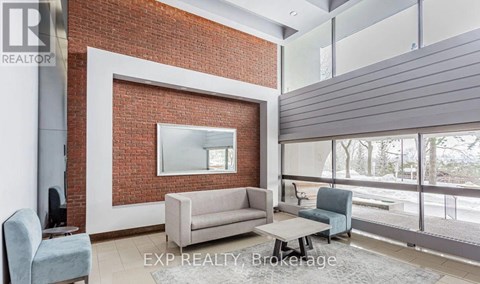 A living room with a grey couch and a red brick wall.