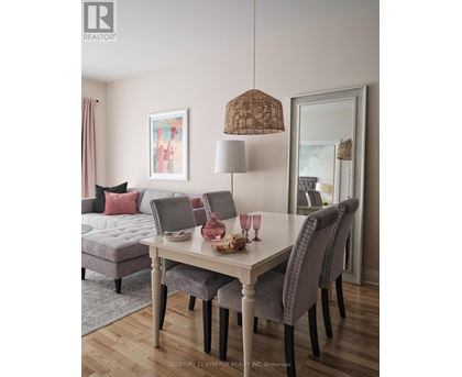 A dining room with a grey sofa, a white table and chairs, and a painting on the wall.