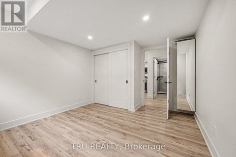 A room with wooden flooring and white walls, with a door leading to another room.