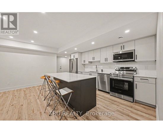 A modern kitchen with wooden flooring and stainless steel appliances.