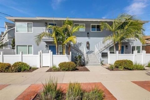 A modern two-story house with a white fence and a palm tree in front.