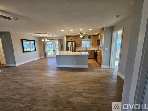 A spacious living room with a kitchen in the background and hardwood floors.