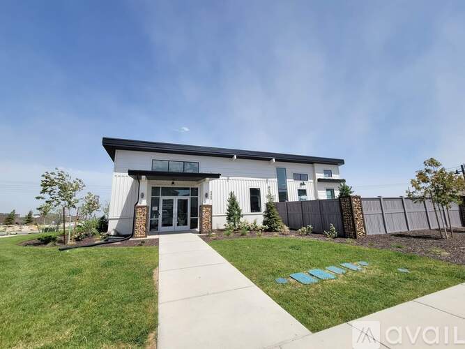 A modern building with a white facade and a black roof is surrounded by a well-manicured lawn and a clear sky.