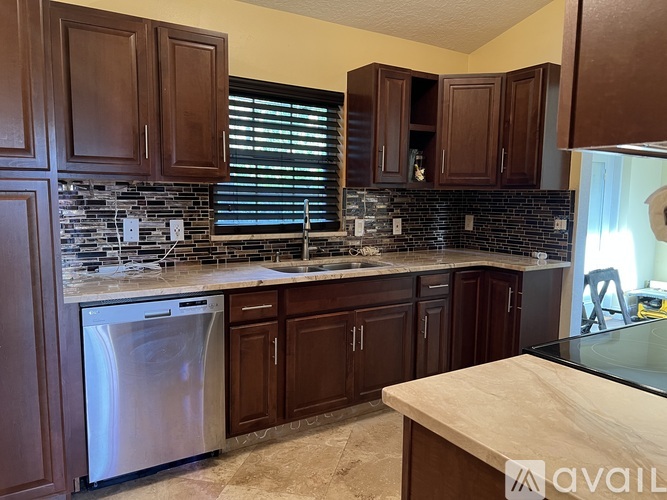 A kitchen with brown cabinets and a black tile backsplash.