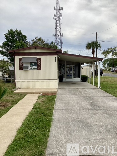 A small building with a brown roof and a white door is surrounded by a concrete walkway and a grassy area.