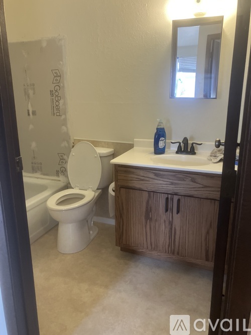 A bathroom with a toilet, sink, and wooden cabinet.