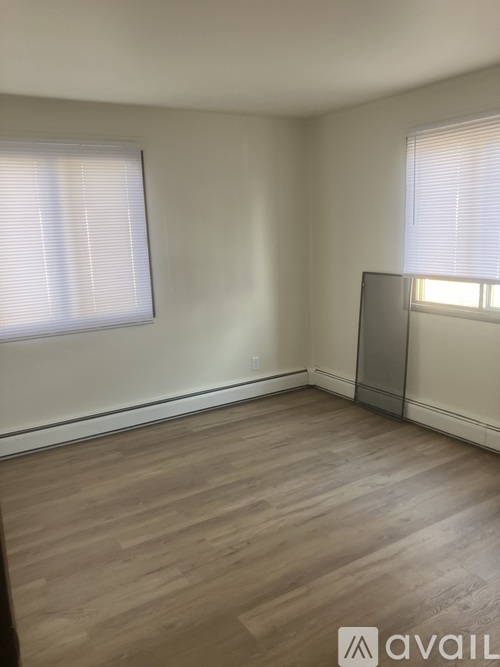 A room with wooden flooring and two windows with blinds.