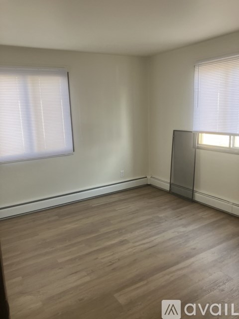 A room with wooden flooring and two windows with blinds.