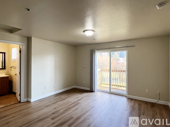 A spacious room with wooden flooring and a sliding glass door leading to a balcony.