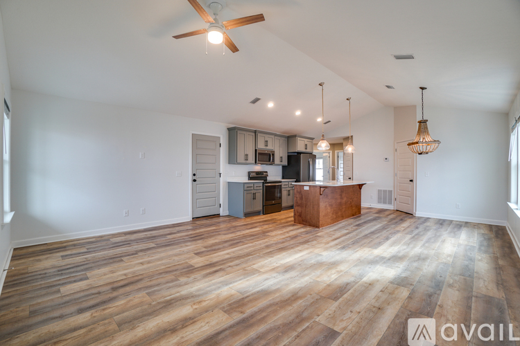 A spacious living room with a kitchen in the background and a wooden floor.