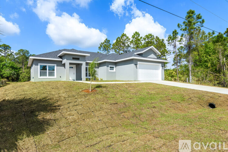 A house with a brown roof and white walls is surrounded by grass and trees.