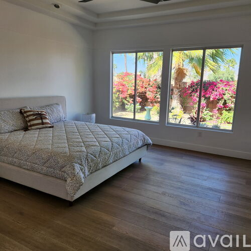 A bedroom with a large bed and a view of a garden through the window.