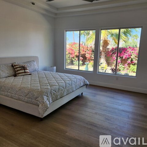 A bedroom with a large bed and a view of a garden through the window.