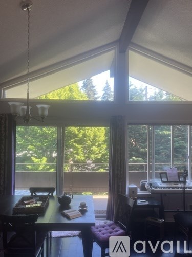 A room with a table, chairs, and a piano with a view of trees outside.