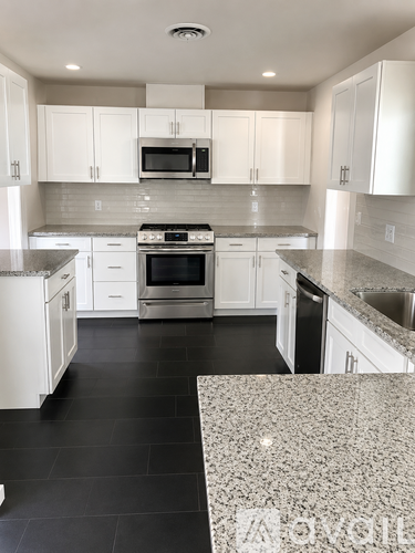 A kitchen with white cabinets and black flooring.