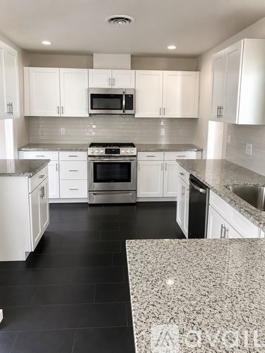 A kitchen with white cabinets and black flooring.