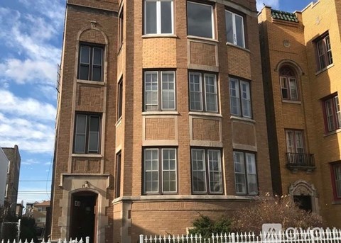 A tall brick building with a white picket fence in front.