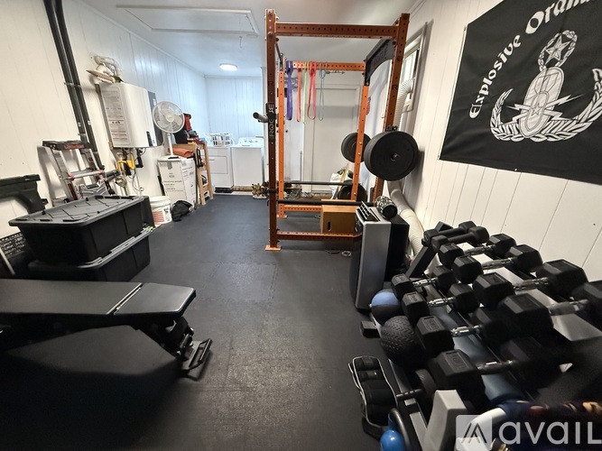 A gym with black flooring and white walls, featuring a variety of exercise equipment.
