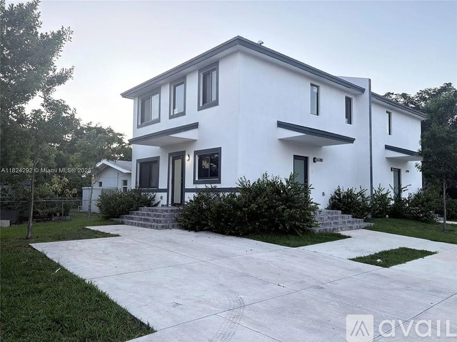 A white two-story house with a black roof and a driveway in front.