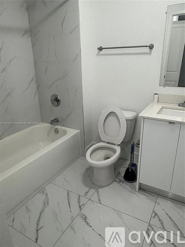 A white toilet is in a bathroom with marble flooring and a white bathtub.