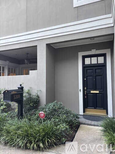 A black door with a gold frame is on the right side of a grey building.