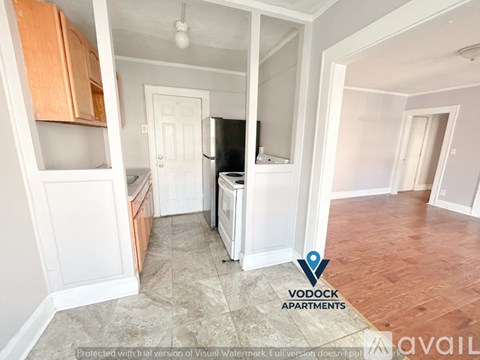 A Vodock Apartments sign is displayed in an empty apartment with a refrigerator, oven, and wooden cabinets.