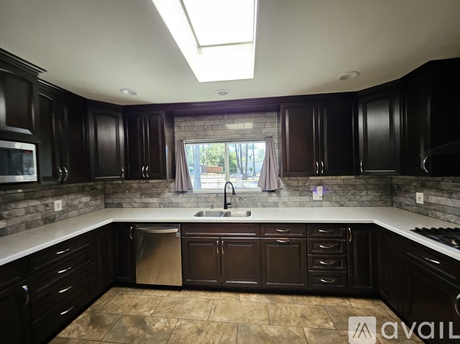 A kitchen with dark wood cabinets and a skylight above the sink.