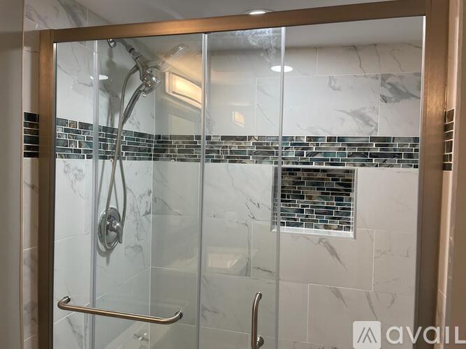 A shower area with a glass door and a silver handle.