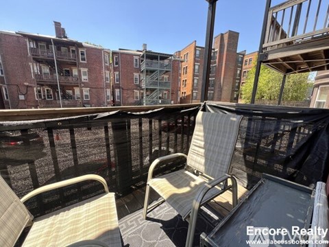 A balcony with two chairs and a table is shown with a view of a cityscape.