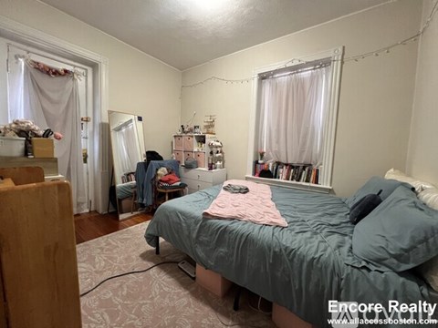 A bedroom with a bed, a window with curtains, and a bookshelf with books.