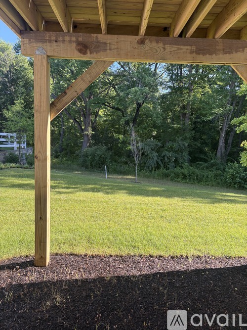 A wooden pergola over a grassy area with trees in the background.
