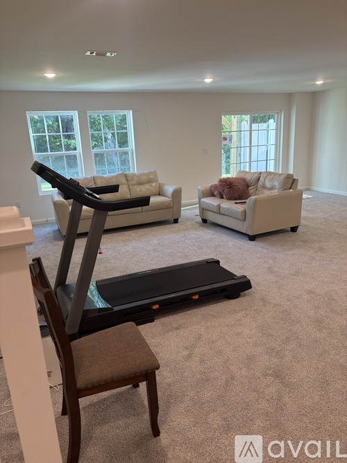 A living room with a treadmill, two couches, and a chair.