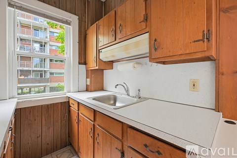 A kitchen with wooden cabinets and a window overlooking a building.