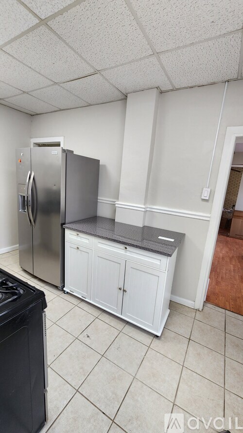 A kitchen with a black trash can, a stainless steel refrigerator, and a white cabinet with a black countertop.