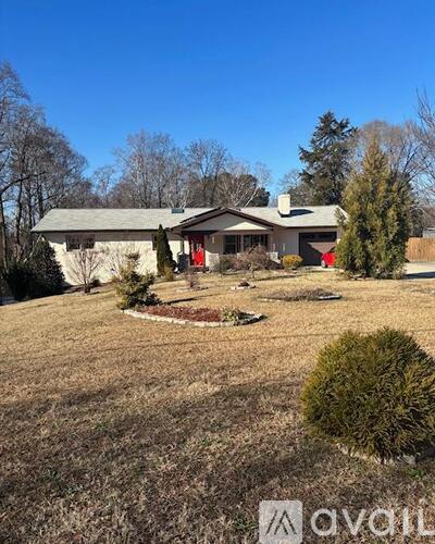 A house with a grey roof and a red door is surrounded by a grassy area and trees.