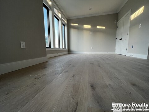 A spacious room with wooden flooring and large windows.
